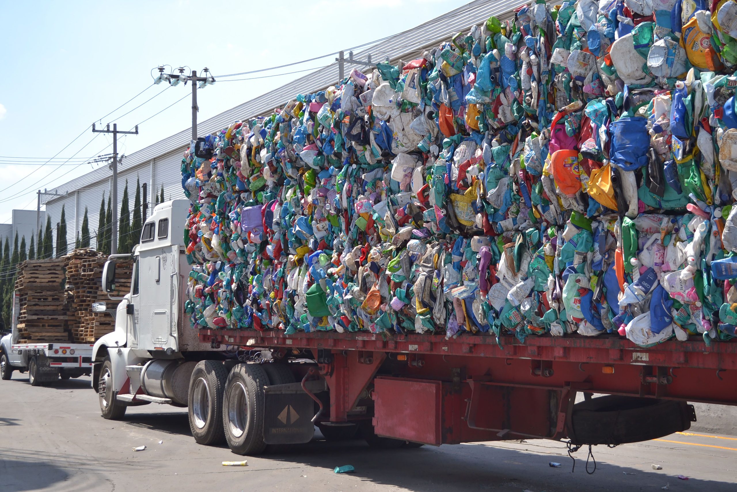 service-1 A large truck carrying bales of compressed plastic waste on a sunny city street in Mexico.
