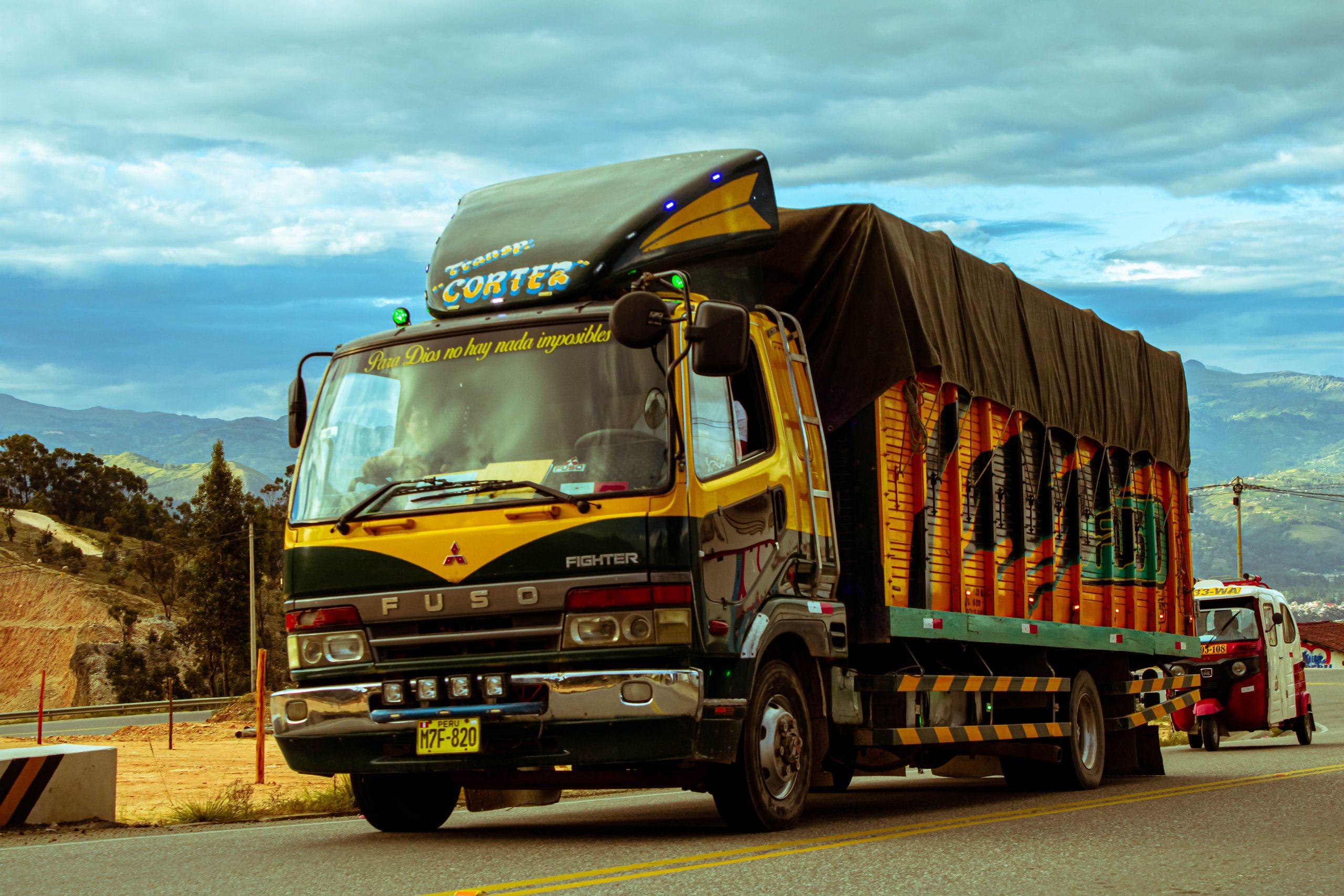 service-1 Vibrant cargo truck cruising a scenic mountain highway under a dramatic sky.